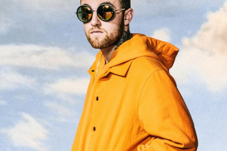 Mac Miller in a bright orange hooded jacket and round mirrored sunglasses, photographed against a pale blue cloudy sky
