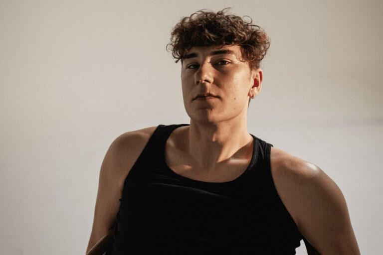BUNT. in a black tank top with curly hair, photographed against a plain pale studio backdrop