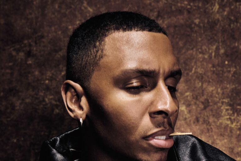 Masego press portrait in a black leather jacket against a brown textured backdrop