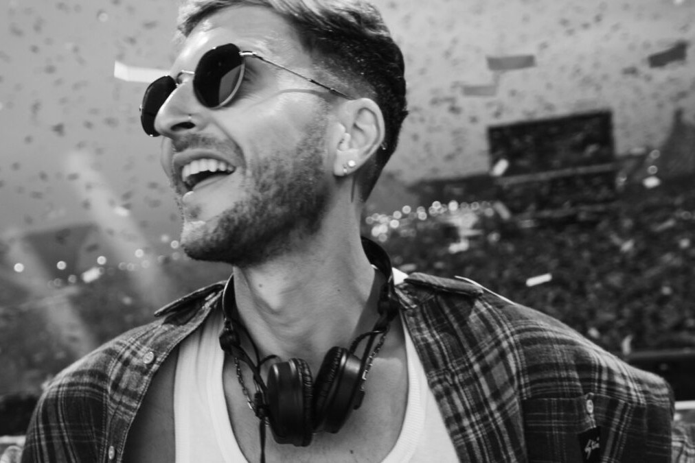 Black-and-white photo of D.O.D smiling and looking up with headphones around his neck as confetti falls over a festival crowd