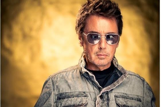 Jean-Michel Jarre press portrait in aviator sunglasses and a denim jacket against a gold backdrop