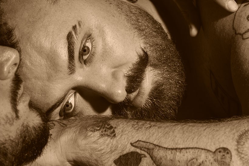 Sepia close-up of Sam Smith's face and tattooed forearm, eyes locked with the camera, for the Hazel Eyes album cover