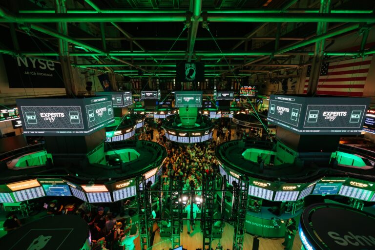 The New York Stock Exchange trading floor lit green, with EXPERTS ONLY displayed across every trading-post screen and a crowd packed into the centre aisle