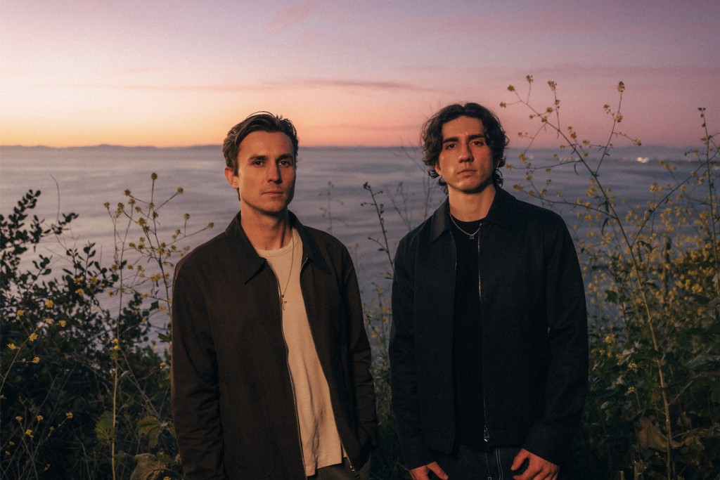 Forester's Xander Carlson and David Parris standing in coastal brush at dusk, ocean and pink sunset sky behind them, both in dark jackets