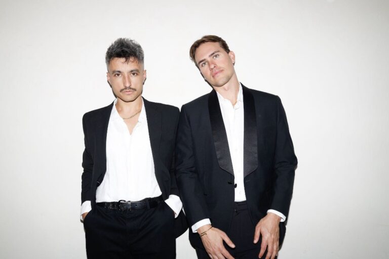 Loud Luxury press portrait: the two members standing side by side in black suit jackets over open white shirts against a plain white backdrop