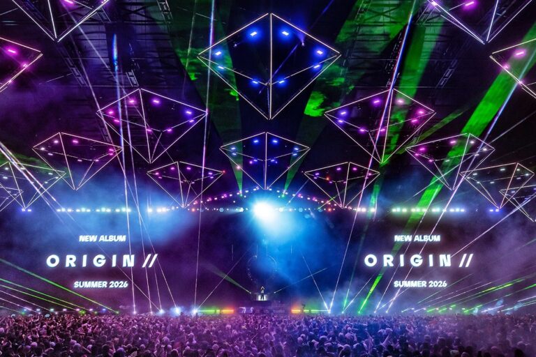 Kaskade performing the ORIGIN // show beneath glowing pyramid light rigs and green lasers, with 'New Album ORIGIN // Summer 2026' on the screens above a packed crowd