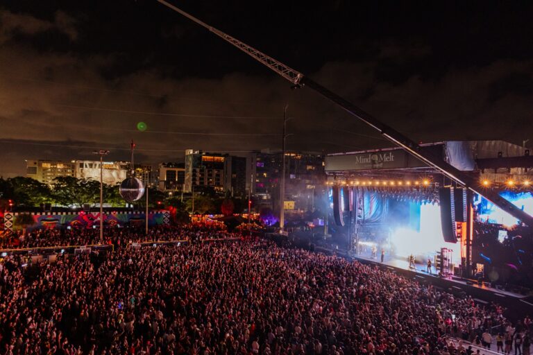 Wide night view of a packed III Points crowd facing the lit-up Mind Melt main stage, with a camera crane arm overhead and Miami buildings behind